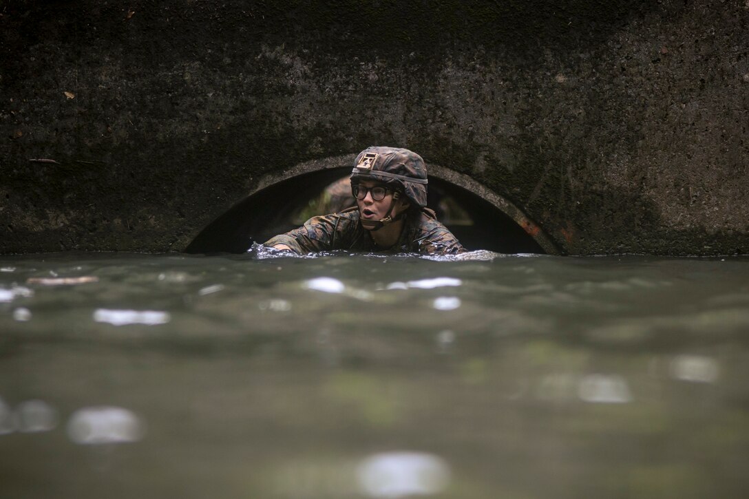 A Marine wearing a uniform swims near a tunnel during an endurance course.