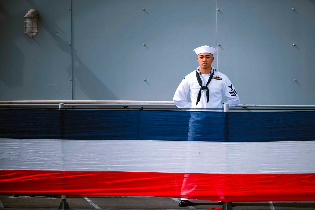 A sailor stands behind a red, white and blue ship covering.