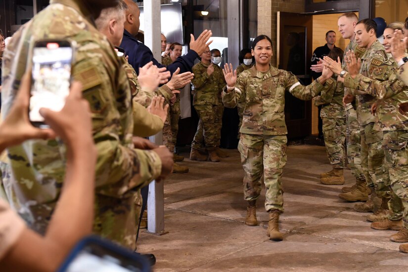 Air Force woman walks down aisle of cheering airmen.