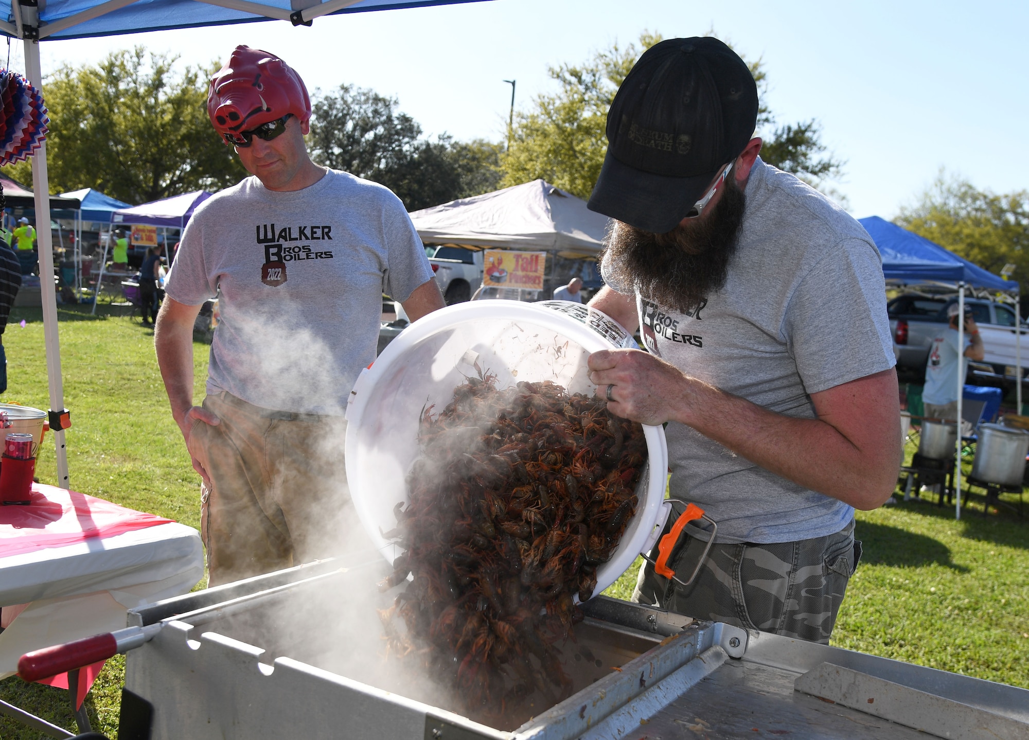 U.S. Air Force Lt. Col. Whitney Walker, 85th Engineering Installation Squadron commander, and his brother, U.S. Coast Guard Retired Electronics Technician 1st Class Wesley Walker, pour live crawfish into a pot of boiling water during the 10th Annual Crawfish Cook-Off at the Bay Breeze Event Center on Keesler Air Force Base, Mississippi, March 25, 2022. More than 20 teams competed in the event and more than 1,500 pounds of crawfish were distributed. (U.S. Air Force photo by Kemberly Groue)