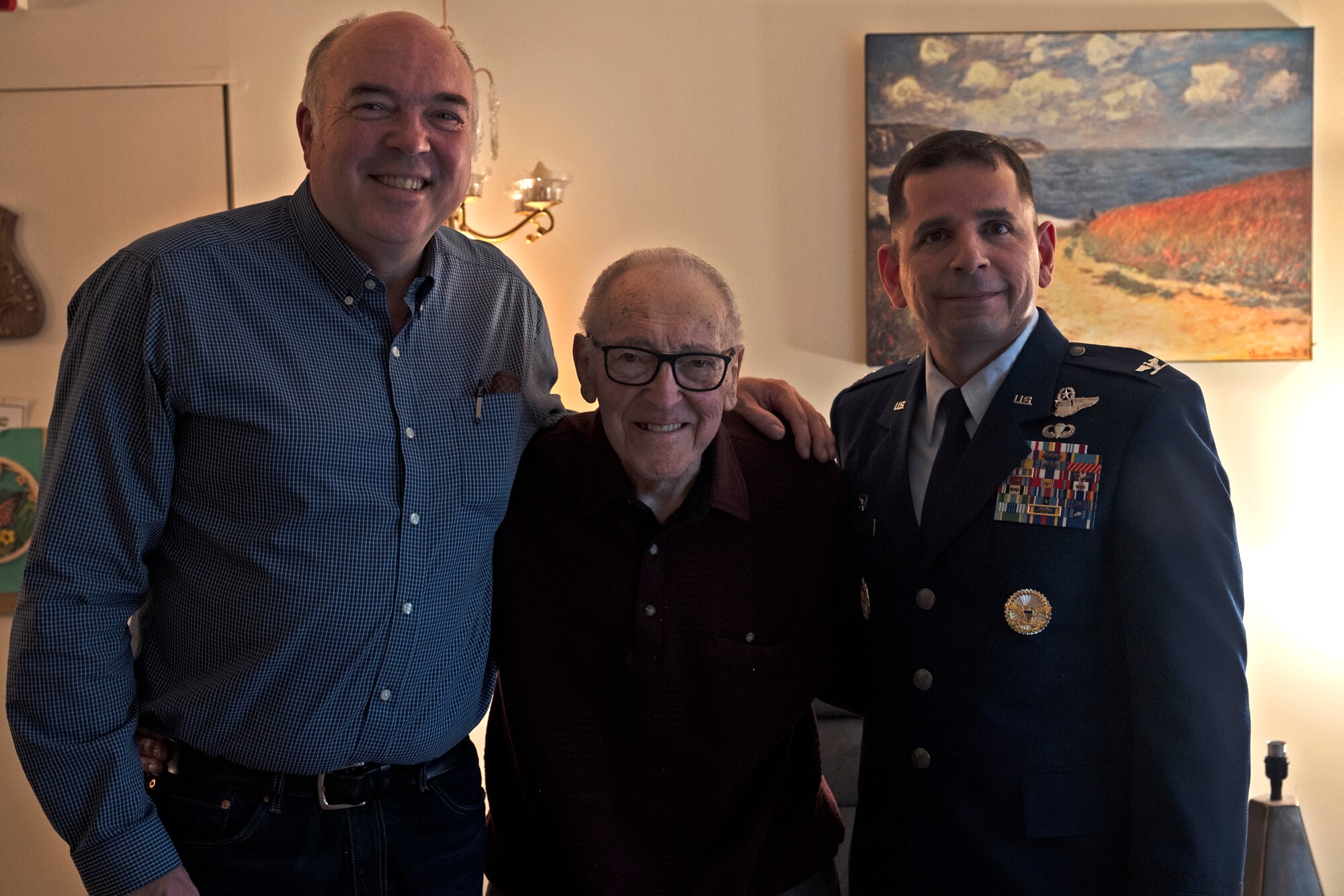(Center) Retired U.S. Air Force Maj. James Slaeker, a WWII pilot, poses for a photo with his son Ted and Col. Sergio Anaya, 62nd Operations Group commander, during a surprise visit from Anaya in celebration of his 100th birthday in Shoreline, Washington, March 25, 2022. Upon becoming a pilot, Slaeker would serve during three wars, including WWII and the Korean War. (U.S. Air Force photo/Senior Airman Zoe Thacker)