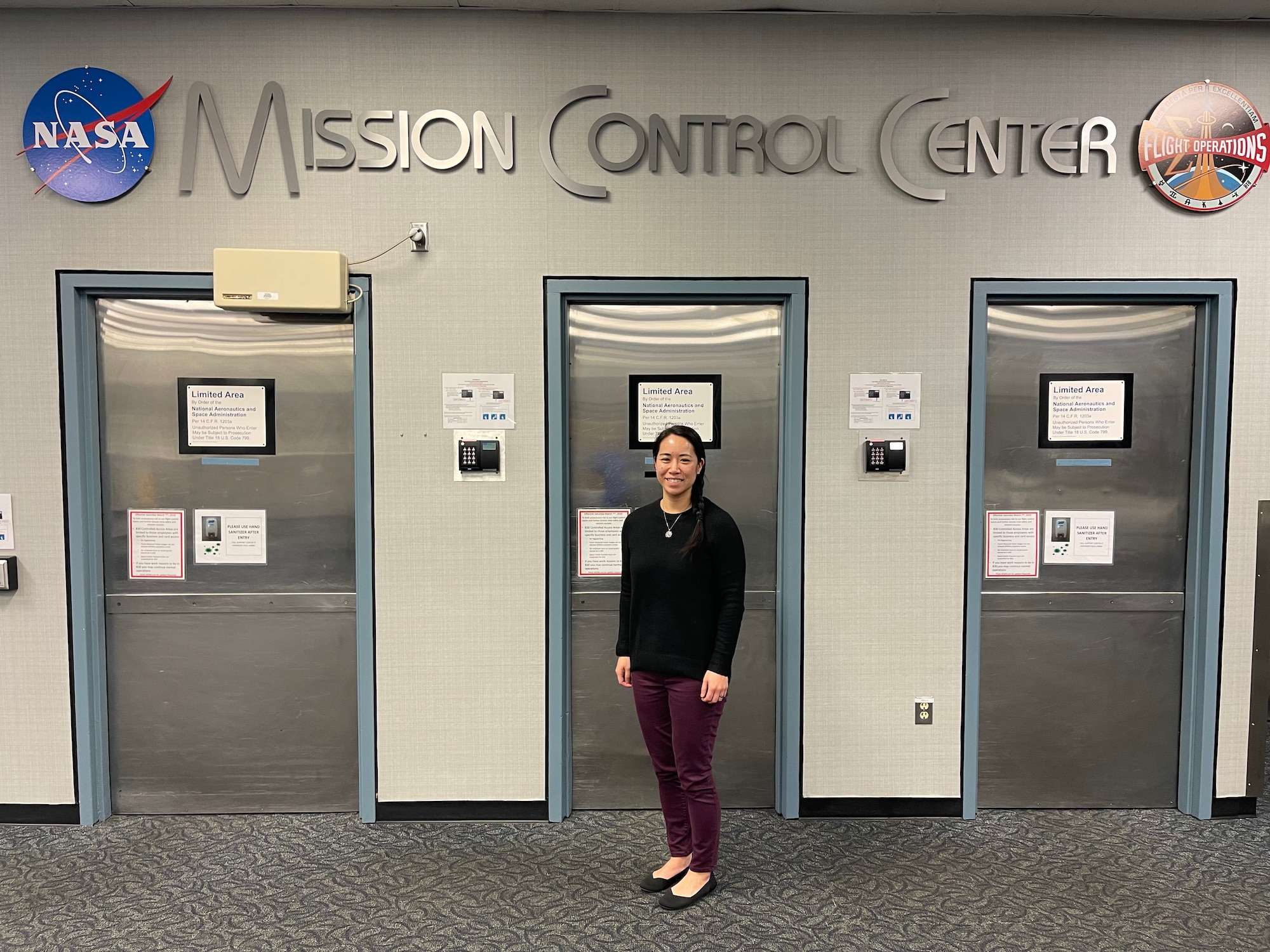 Three silver doors with Mission Control Center above them. Maj. Hirai stands in front of the middle door