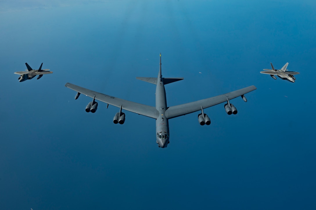 A B-52H Stratofortress flies over the Arabian Gulf with an F-22 Raptor on each side.