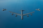 A B-52H Stratofortress flies over the Arabian Gulf with an F-22 Raptor on each side.