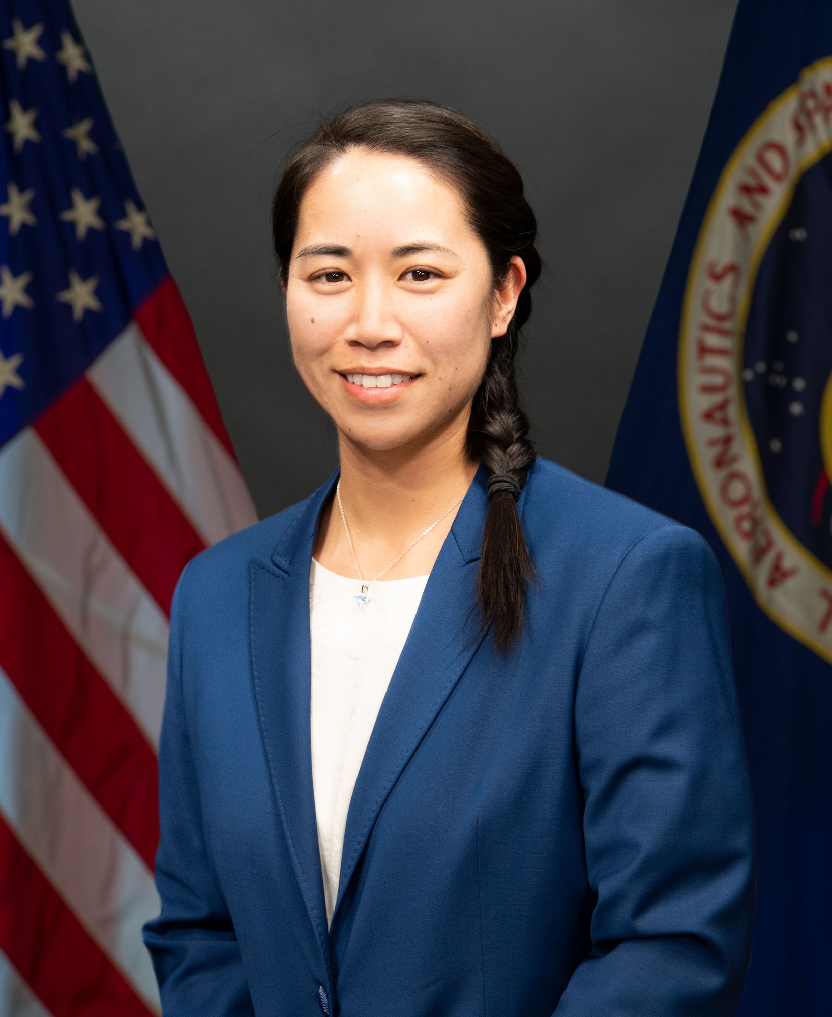 Joyce Hirai poses in the middle of the photo flanked by a US flag and a NASA flag