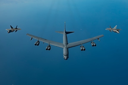 A B-52H Stratofortress flies over the Arabian Gulf with an F-22 Raptor on each side.