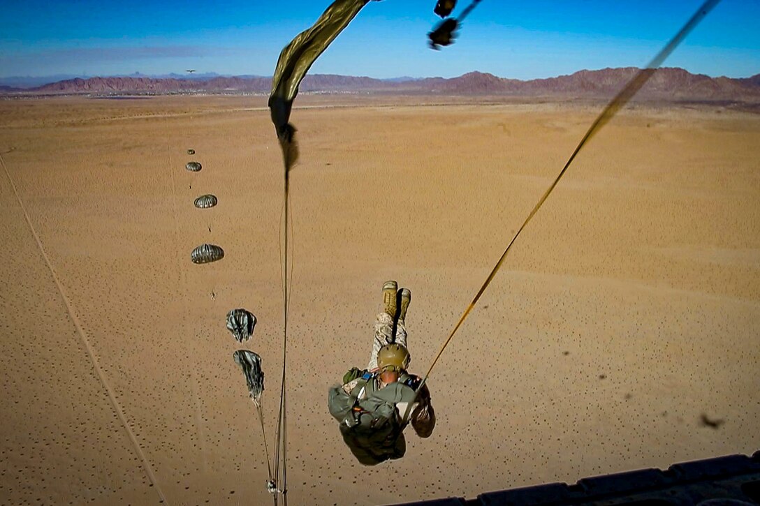 Marines wearing parachutes jump out of an airborne aircraft.