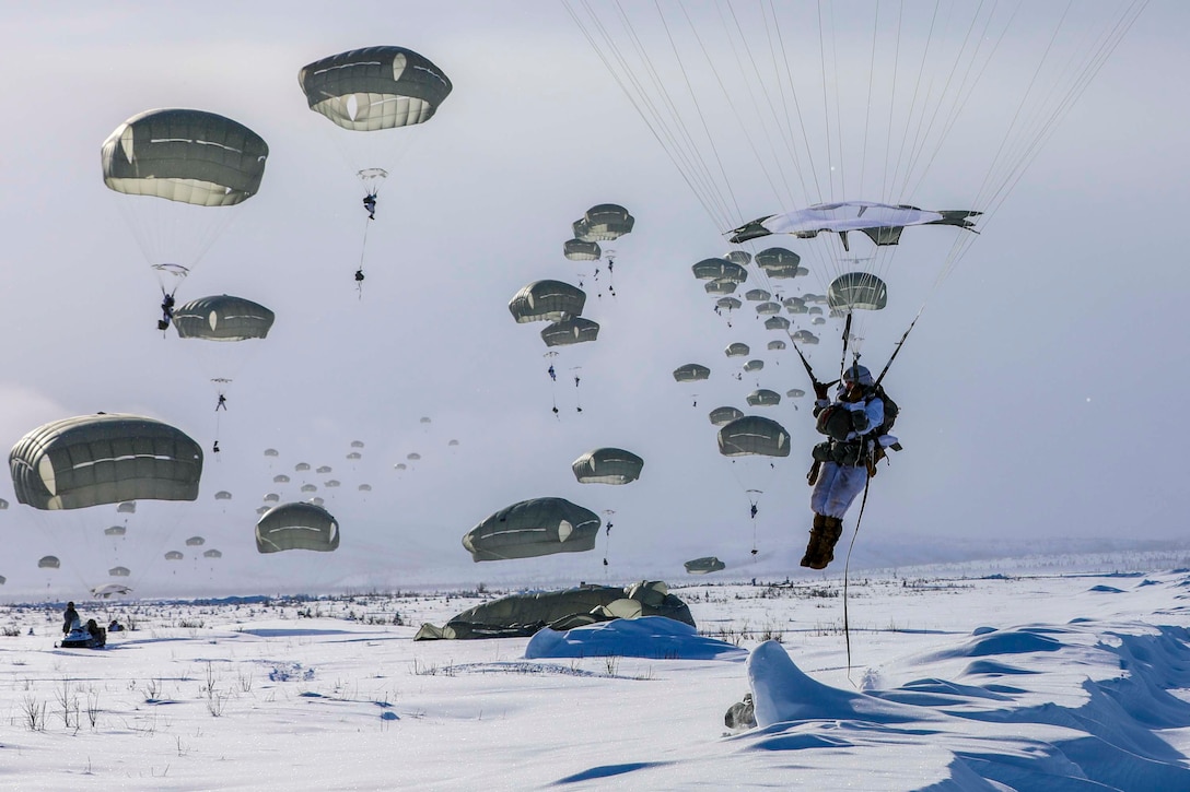 Soldiers descend in the sky onto a snow-covered ground while wearing parachutes.