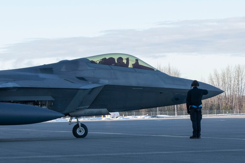 An Airman stands in front of and directs an F-22 aircraft