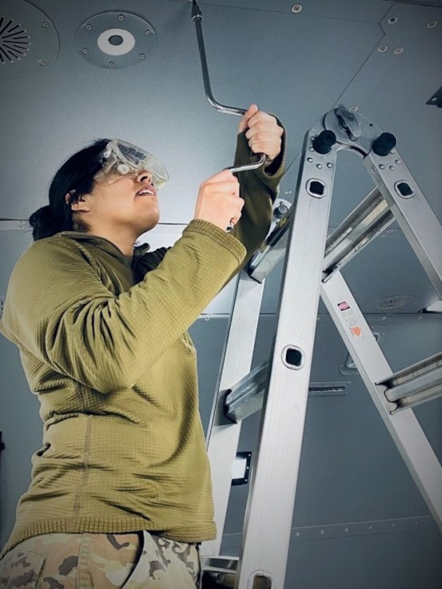 Senior Airman Xochitl Hernandez stands on a later and removes a ceiling panel on a KC-46 Pegasus.