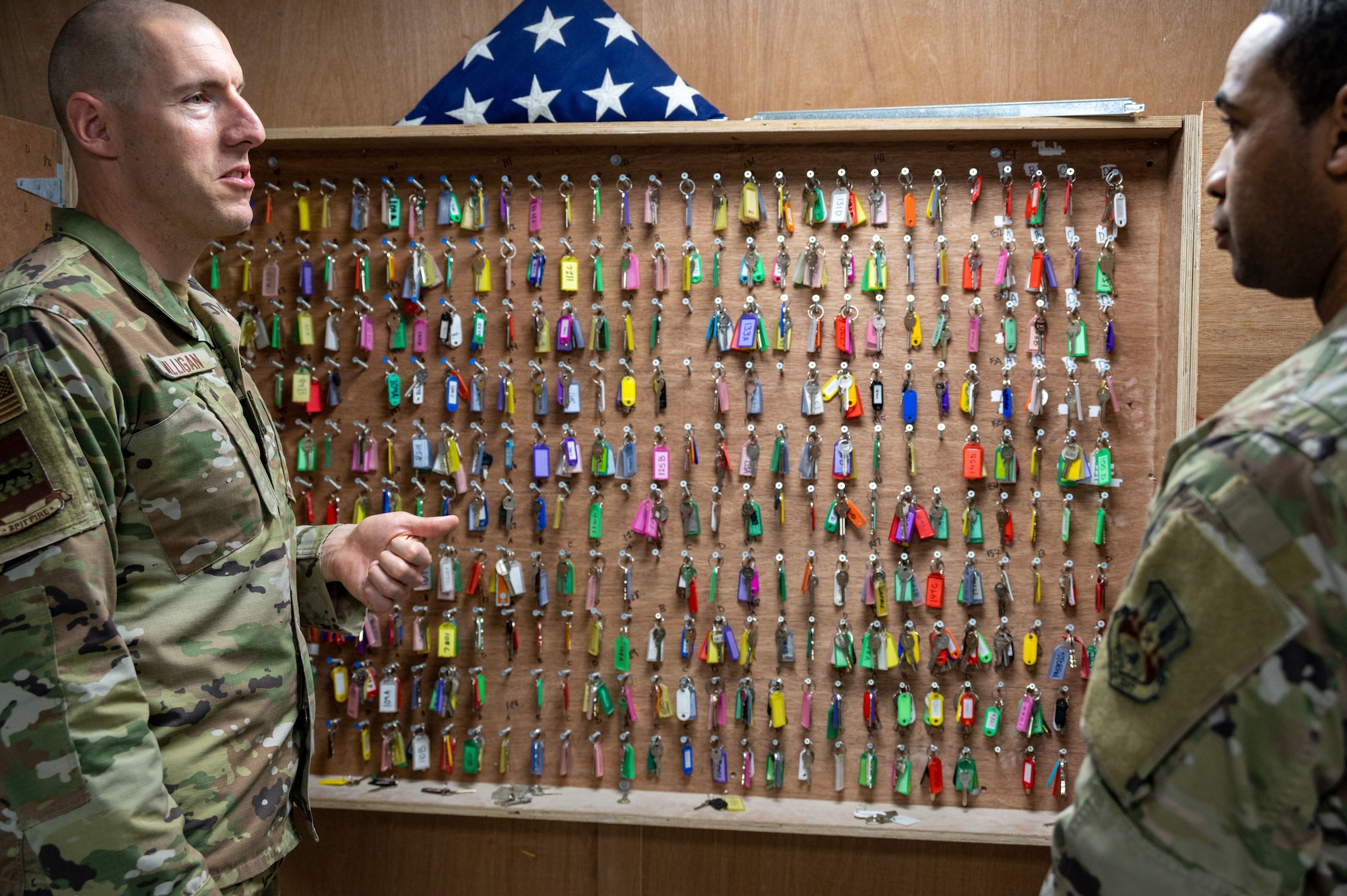 U.S. Air Force Chief Master Sgt. Sean M. Milligan, 332d Air Expeditionary Wing command chief, talks with 332d Expeditionary Force Support Squadron Lodging Flight Staff Sgt. Quinton Townsend in front of a wall of lodging keys at an undisclosed location in Southwest Asia March 26, 2022. Chief Milligan's immersion visits give him a better understanding of the unique skillsets every Airman brings to the 332d AEW Red Tail team. (U.S. Air Force photo by Tech. Sgt. Lauren M. Snyder)