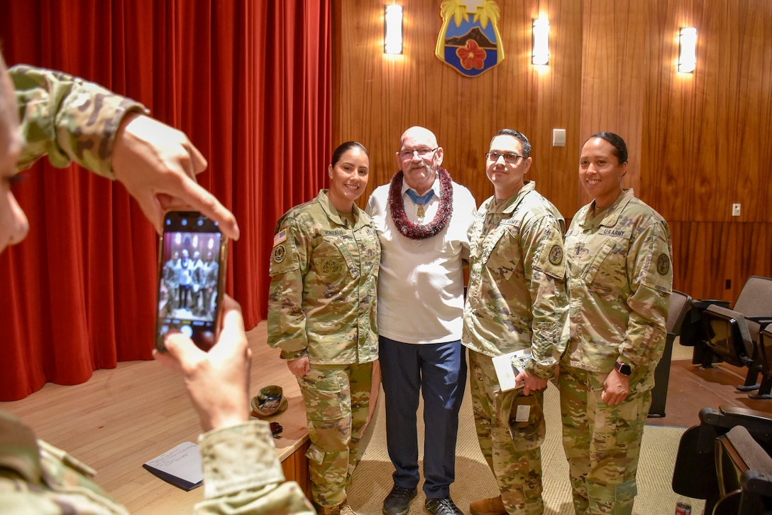 An older man poses with three soldiers in uniform for a photo.