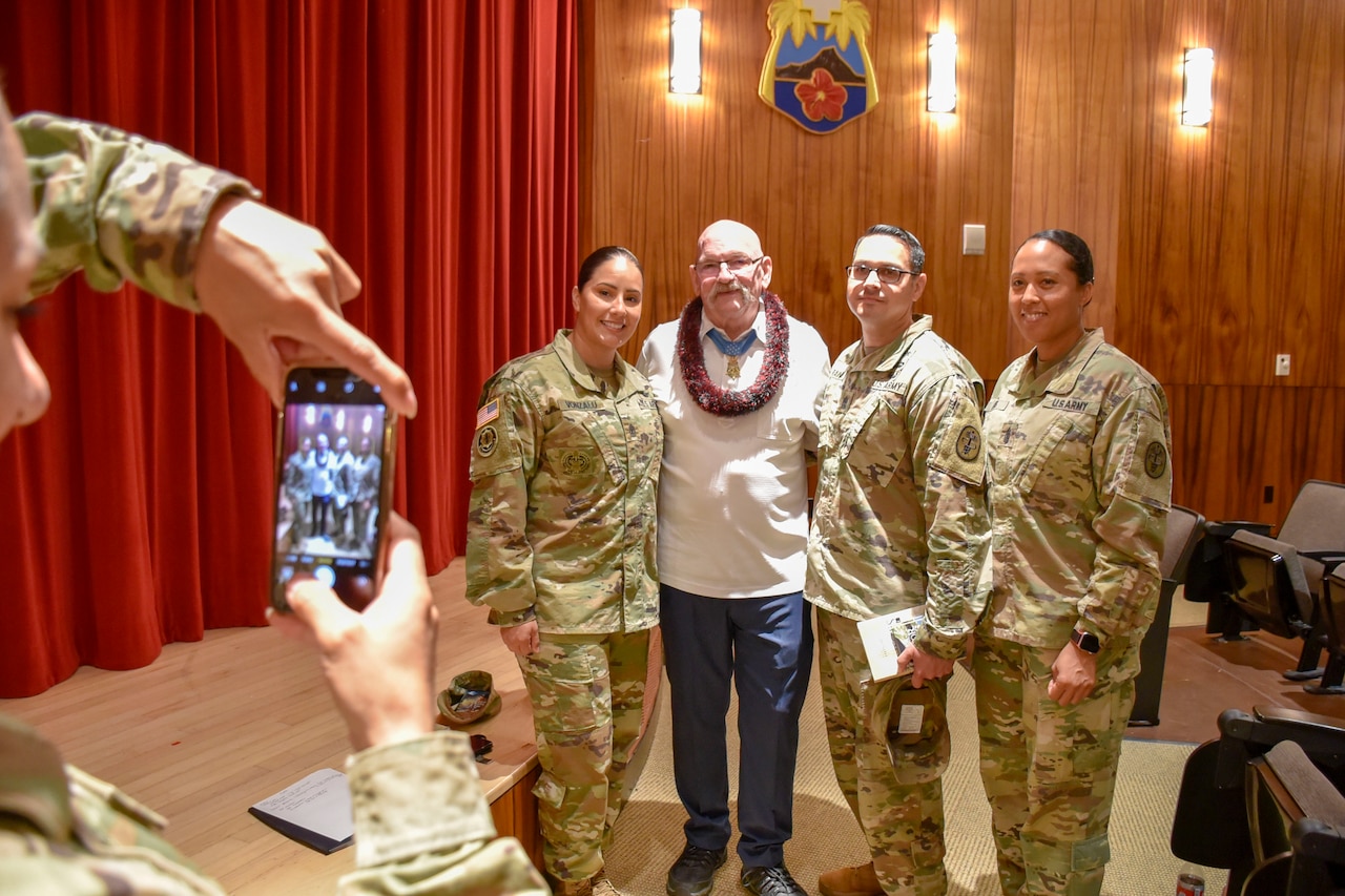 An older man poses with three soldiers in uniform for a photo.