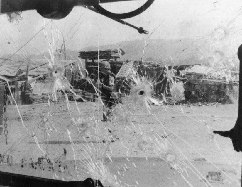 A man is seen standing in the open through bullet-shattered glass.