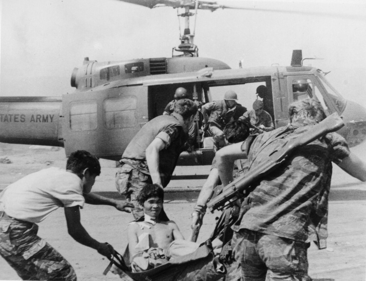Several men rush a wounded boy in a stretcher toward a helicopter.