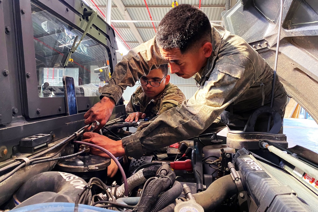 Two soldiers work on a military vehicle.