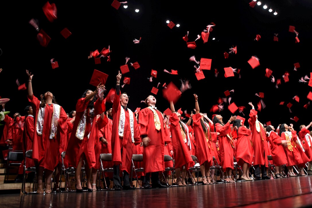 Students in red graduation gowns toss caps in the air.