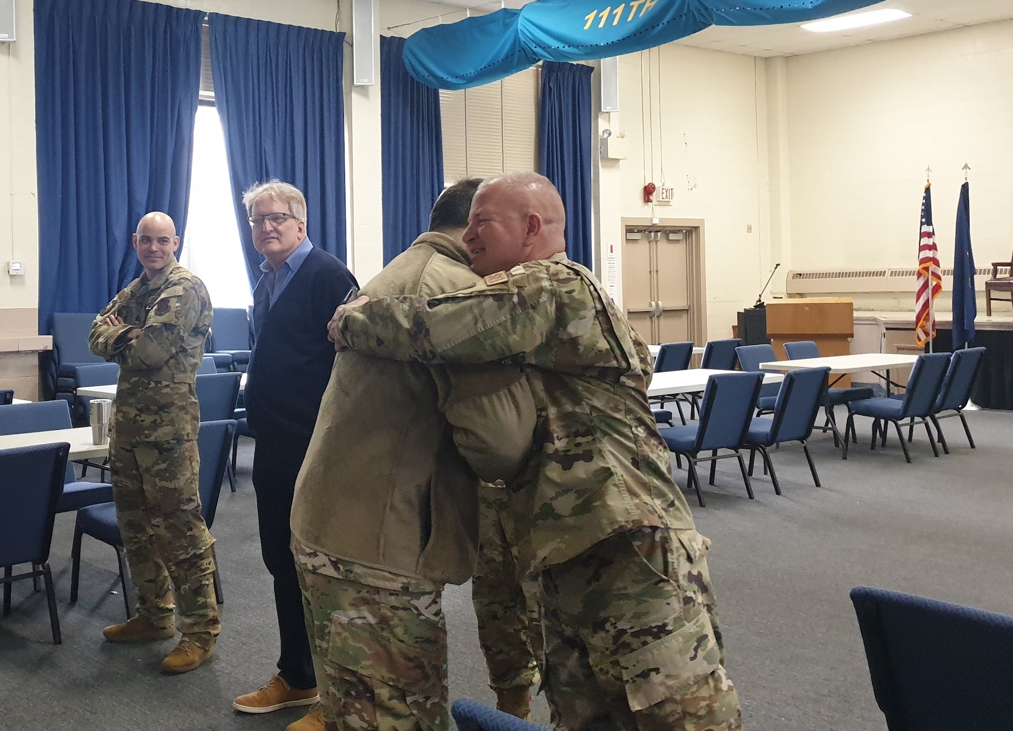 Two men in military uniforms greet each other with a hug.