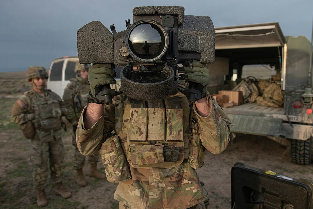 A soldier uses a missile targeting system during training as fellow soldiers watch.