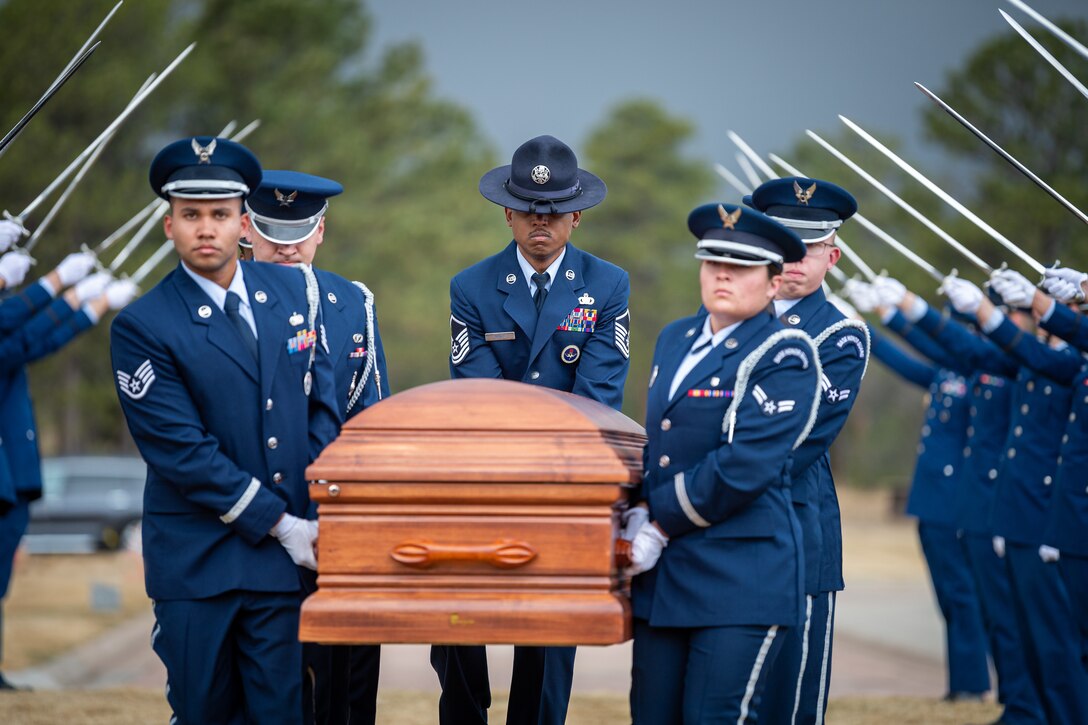 Airmen carry a casket under an arch of sabers.