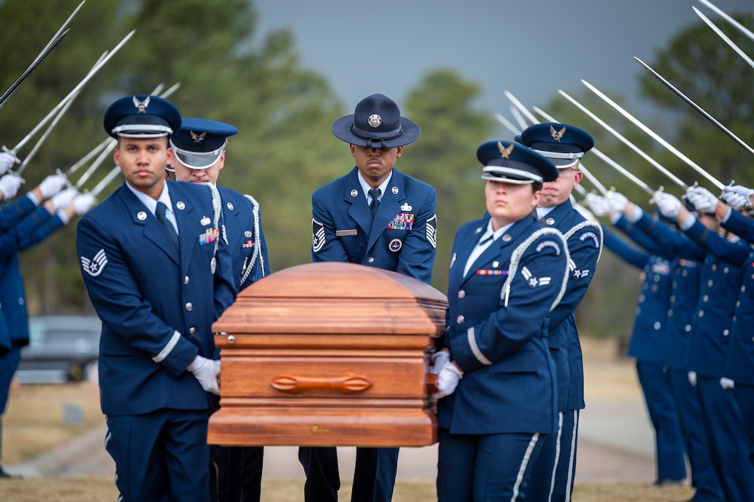 Airmen carry a casket under an arch of sabers.