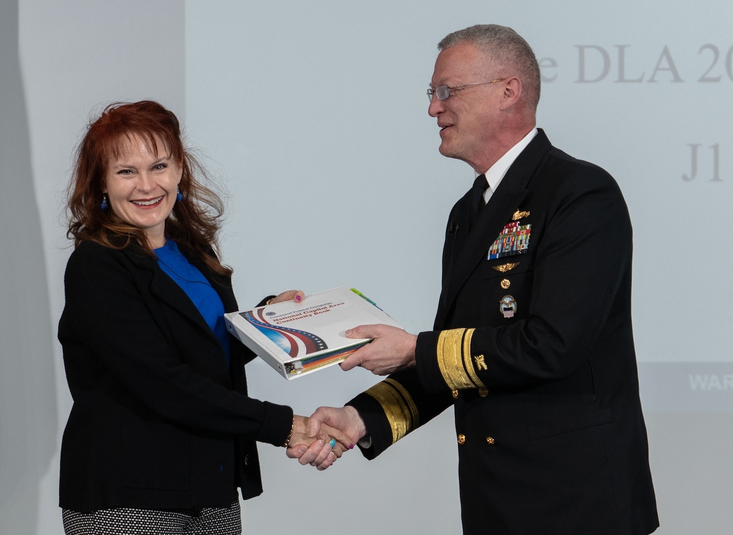 Navy Rear Adm. Grafton Chase, director of the DLA Joint Reserve Force and DLA CFC vice chair, passes the CFC campaign book to Sharyn Saunders, DLA Human Resources director and chair of the 2022 CFC campaign.  (Photo by Christopher Lynch, DLA Graphics-Multimedia Division)