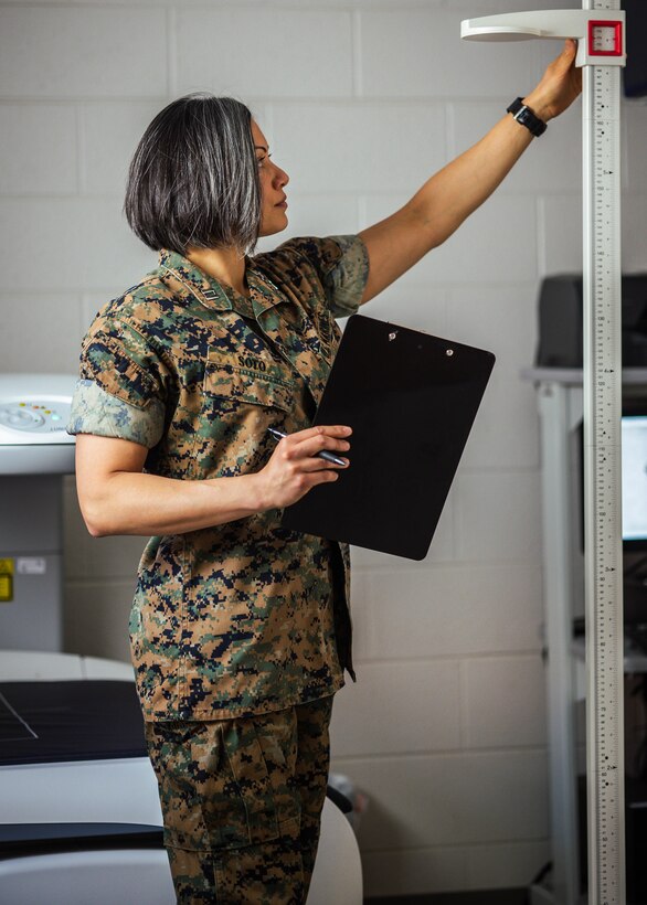 A Marine stands and holds a clipboard while looking at equipment.