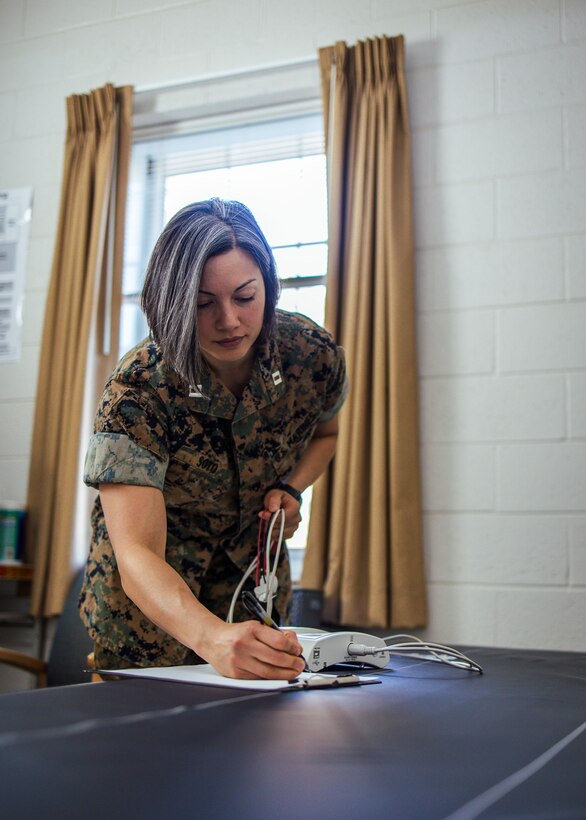 A Marine stands and writes something on a paper on a table.