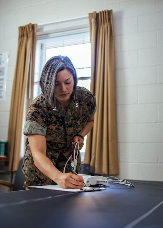 A Marine stands and writes something on a paper on a table.