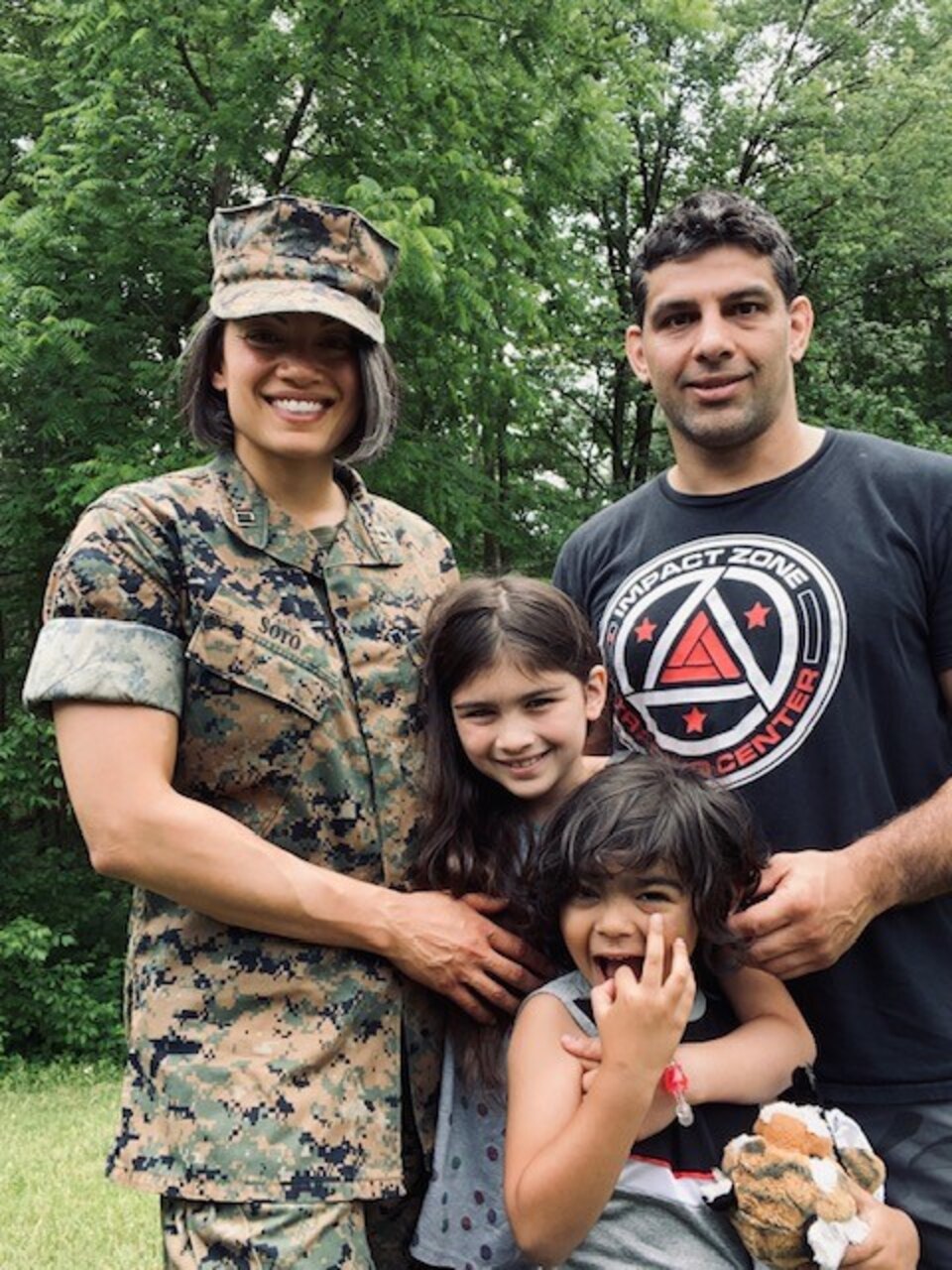 A Marine and another adult smile for a photo outside with two children.