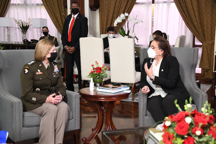 A woman wearing a military uniform and a woman dressed in civilian clothing sit in armchairs facing one another.