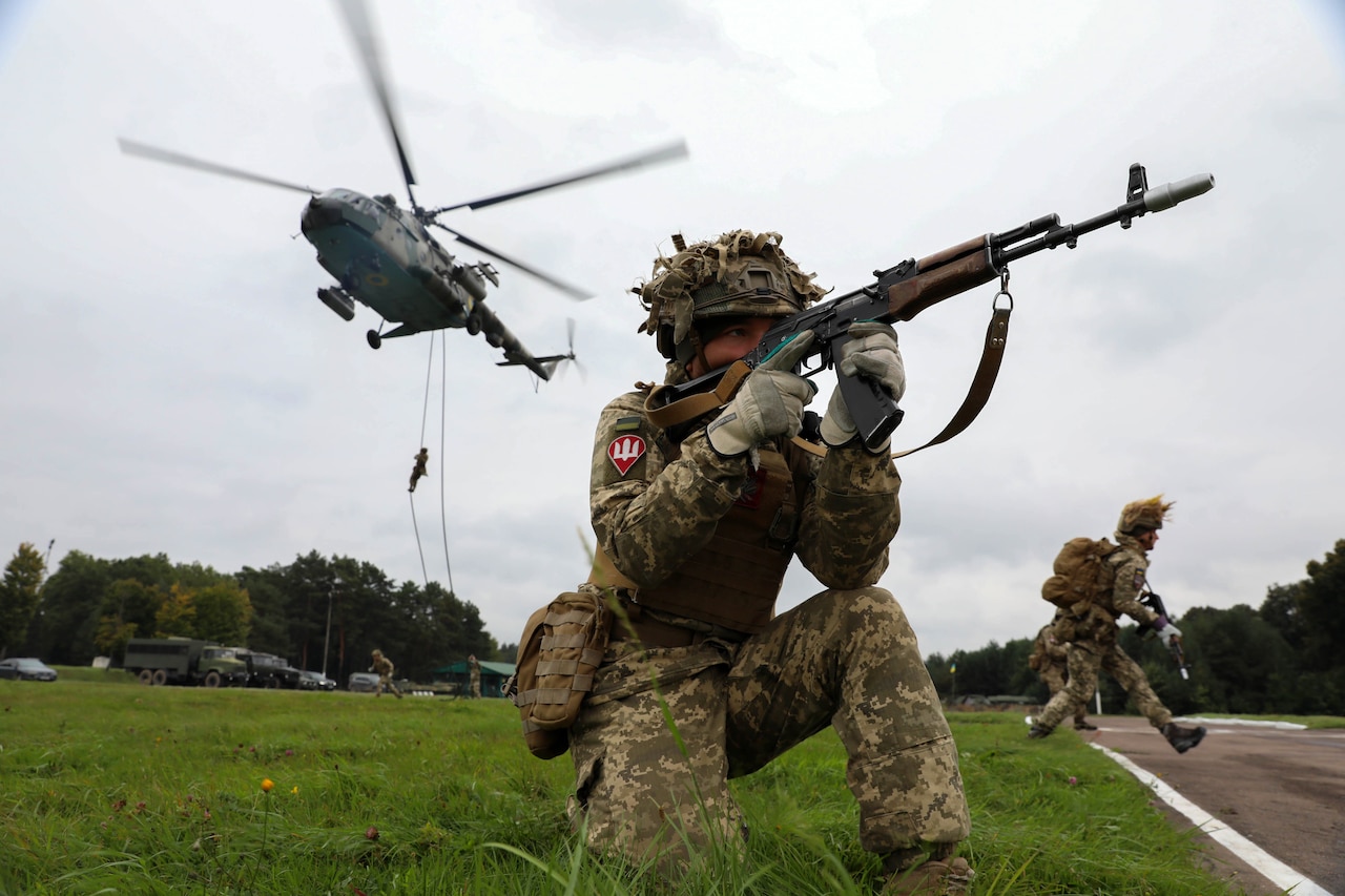 A soldier with a rifle stands guard as fellow a soldier descends from a helicopter.