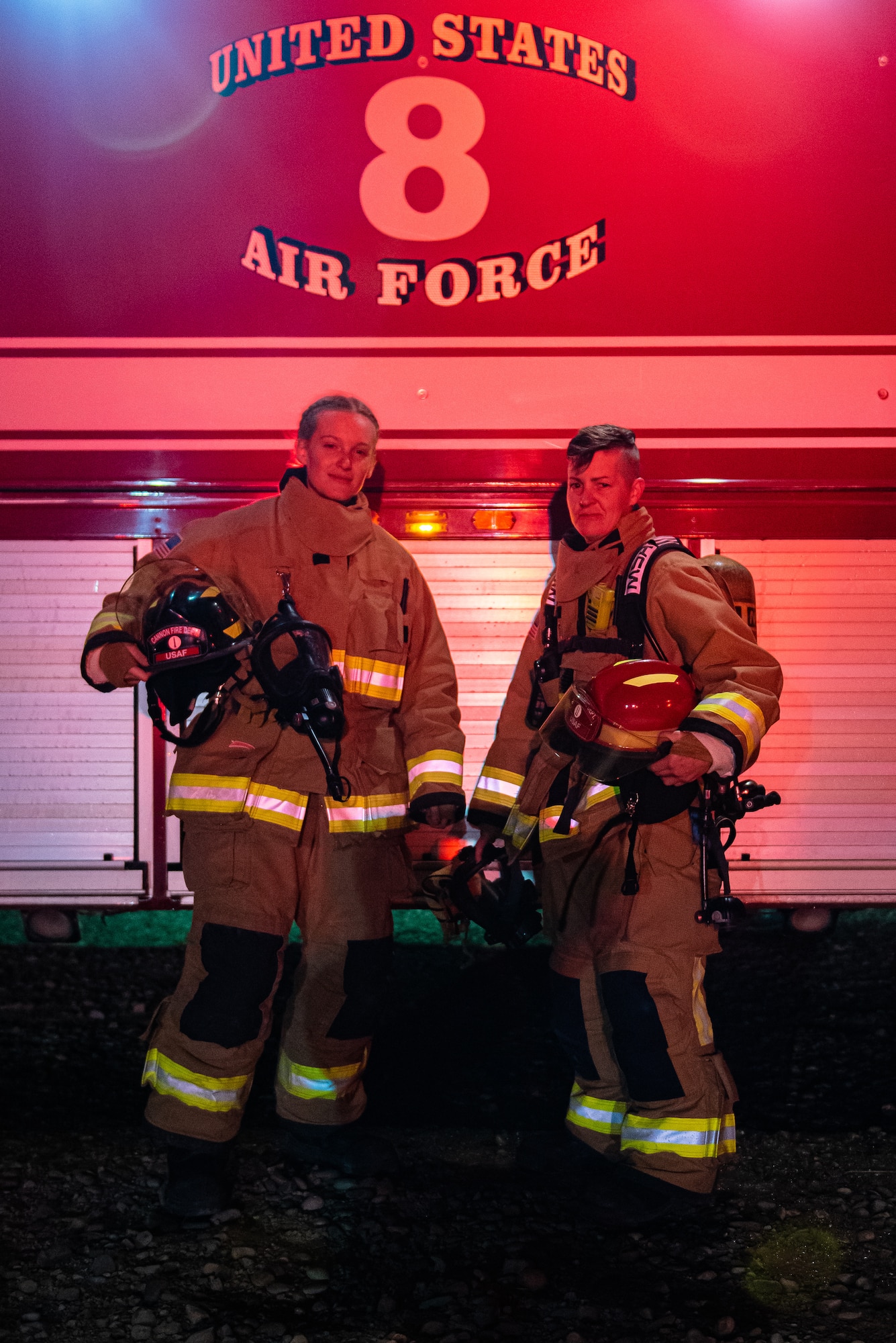 Two firefighters posed for a portrait on the side of their fire truck.