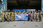 A group of people holding a banner stand for a photo on the deck of a ship.