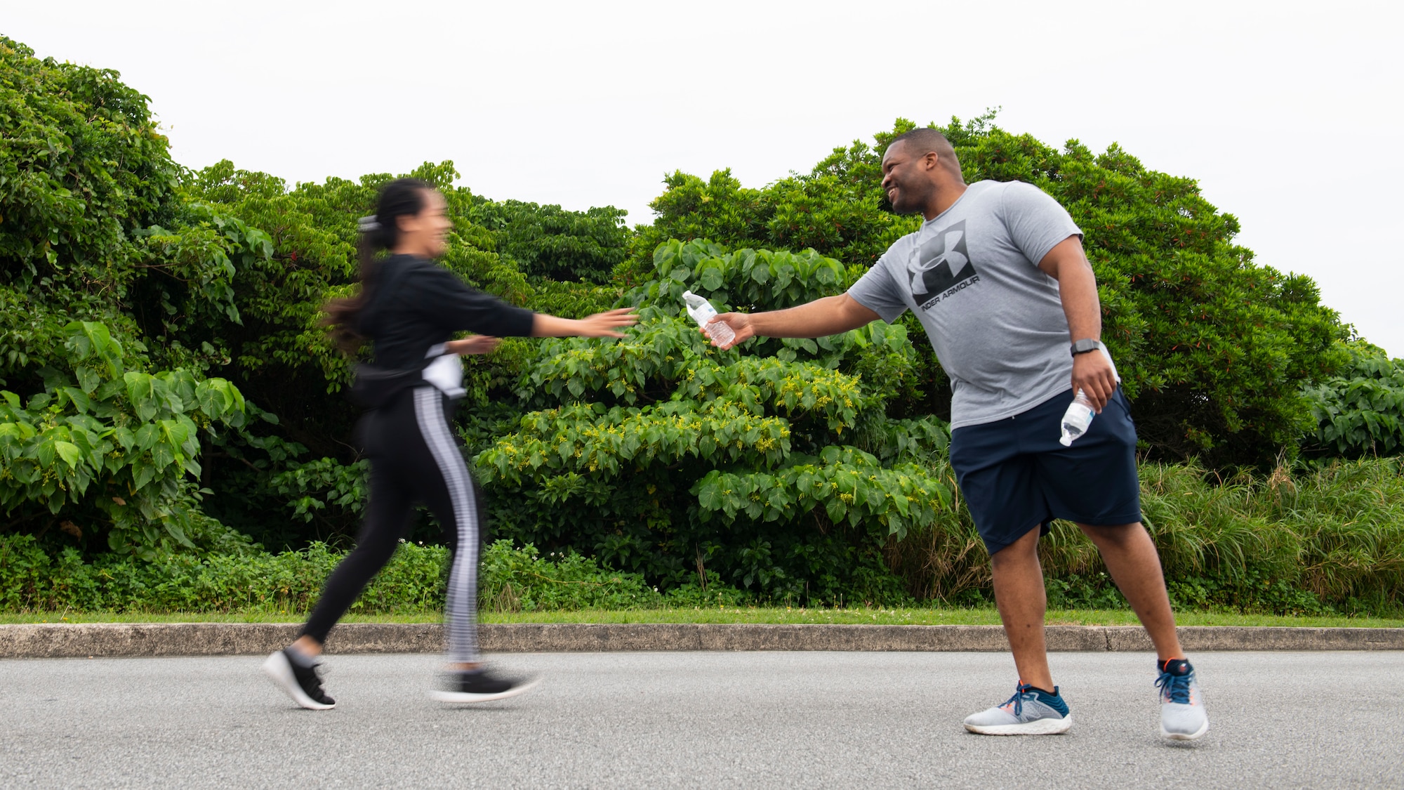 Master Sgt. Piankhy Richberg, 18th Wing Equal Opportunity Office deputy director, hands a water bottle to a runner during the 9th Annual Memorial for the Bataan Death March at Kadena Air Base, Japan, April 23, 2022. There were six water stations set up throughout the 8.5-mile route around the 18th Wing flightline. (U.S. Air Force photo by Senior Airman Jessi Monte)