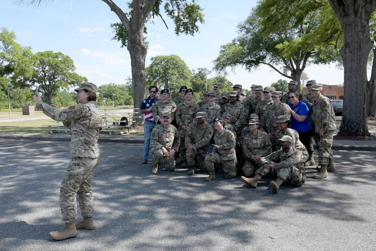 Airman taking a selfie with a group of Airmen behind her posing in the photo.