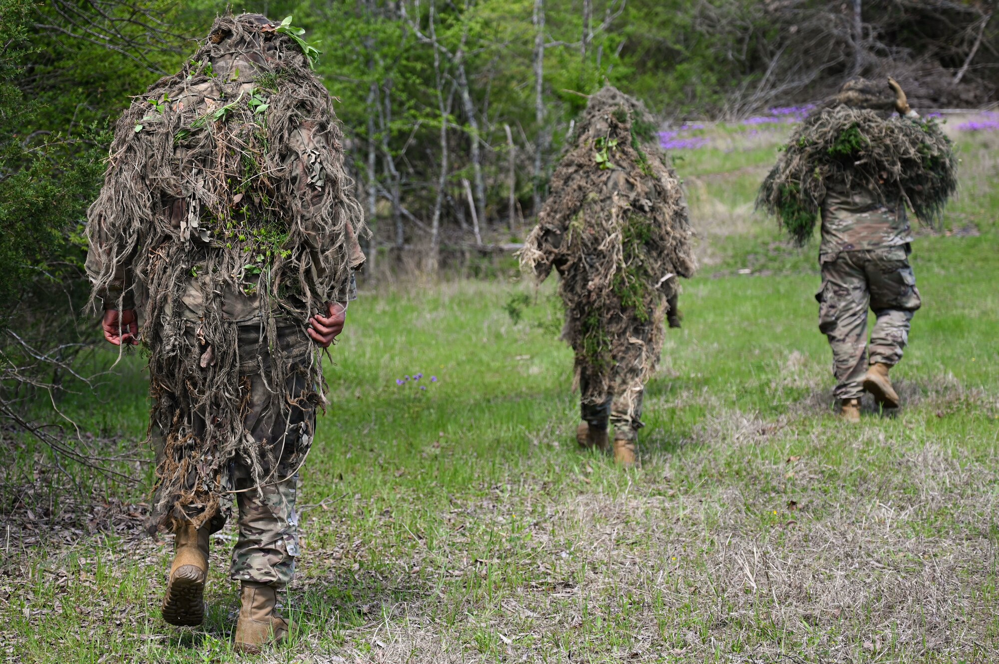 Airmen from the 19th Security Forces Squadron walk through a field during an Advanced Designated Marksman course