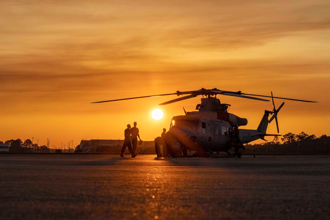 Marines walk toward a helicopter under a sunlit sky as shown in silhouette.