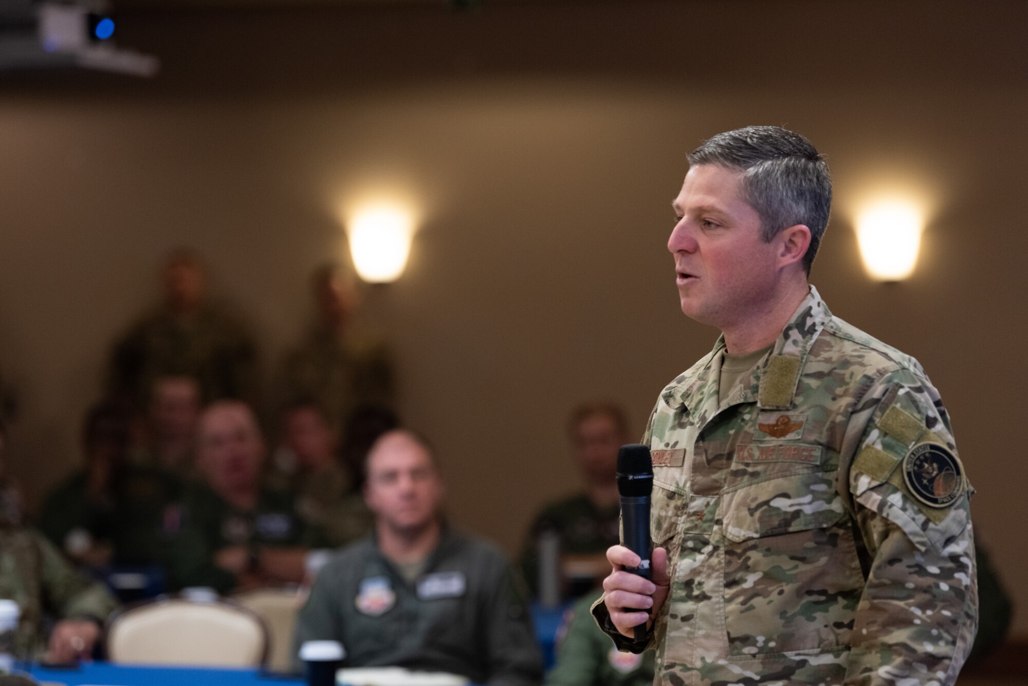 A General speaks through a microphone to a room of Airmen and Guardians.