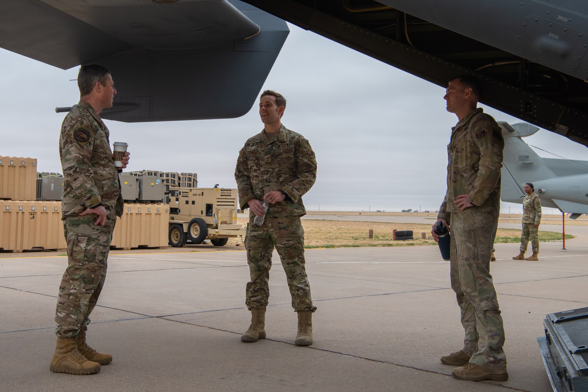 Three Airmen stand and chat behind a CV-22 Osprey.