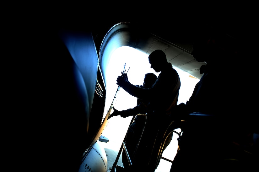 Service members remove a panel from the side of an aircraft.