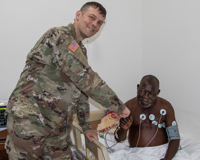 U.S. Army Capt. Matthew Gomberg, a battalion physician assistant assigned to Headquarters and Headquarters Company, 3rd Battalion, 126th Infantry Regiment (3-126th IN), Michigan National Guard (MING) stands with a cardiac patient in 14 Military Hospital in Monrovia, Liberia April 26, 2022. The man had died the day before, but MING's medical team assisted hospital staff to bring him back to life. MING's State Partnership Program with Liberia was on full display as various medial units conducted a medical "best practices" exchange in Monrovia April 25-29, 2022, at the hospital. Together with the AFL, MING helped establish the facility in September 2021, making it the country's first military hospital. (U.S. Army National Guard photo by Capt. Joe Legros)