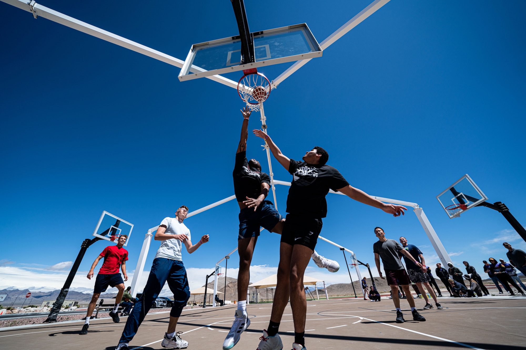 An airman goes up for a lay-up during a basketball game and is defended by two other Airmen under the basketball hoop.