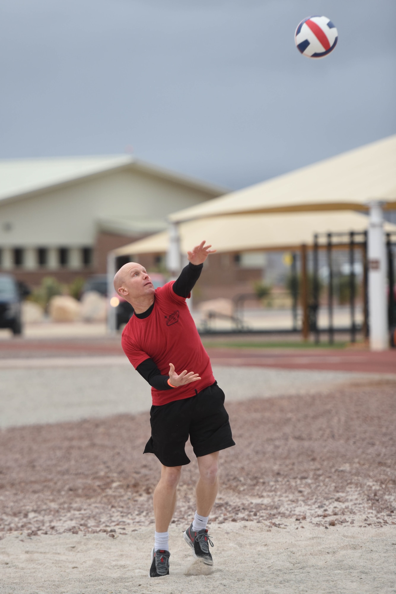 An airman throws a volleyball up in the air and hits it to serve during a volleyball game.