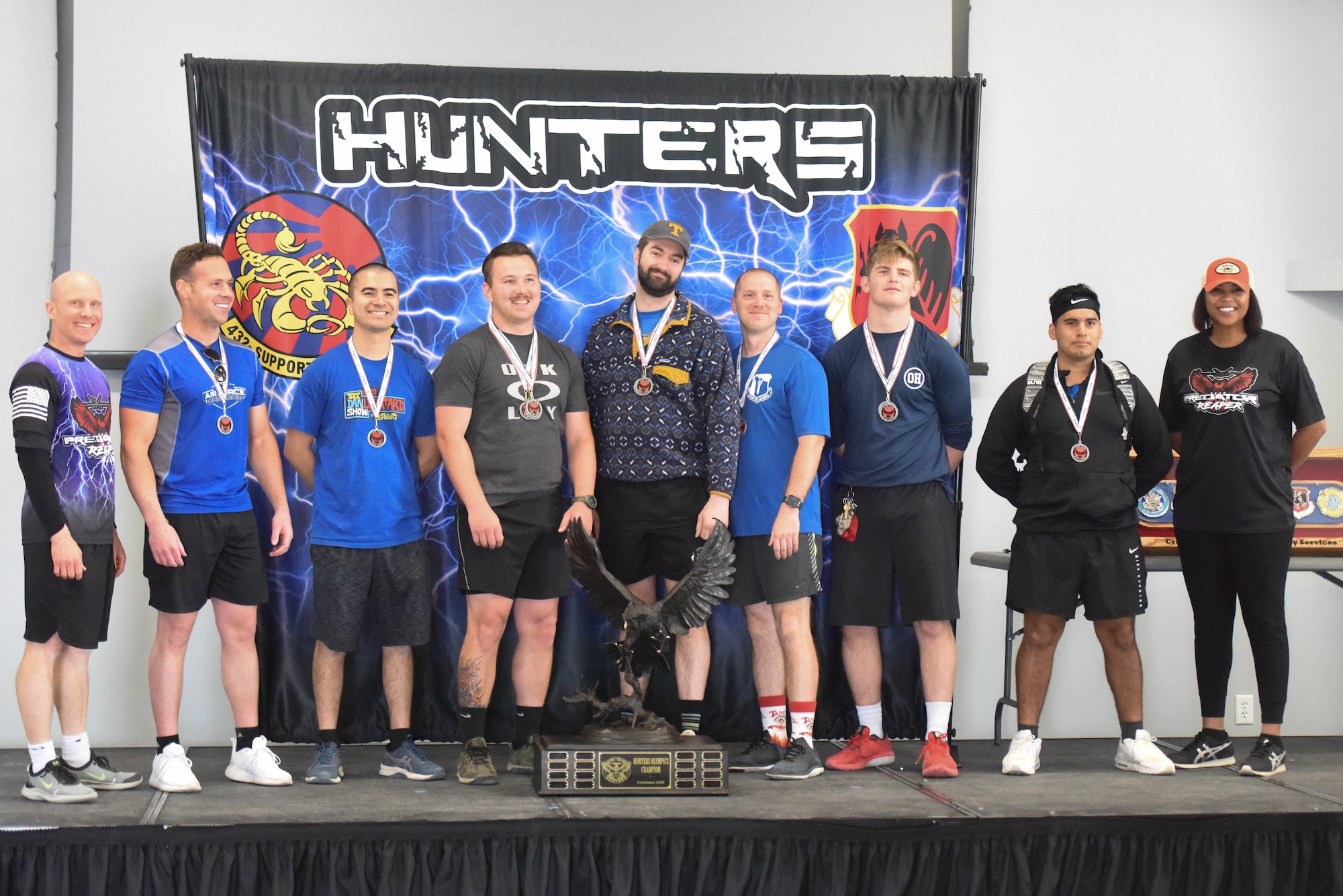 A group of Airmen stand on stage with the Hunter Olympics trophy.