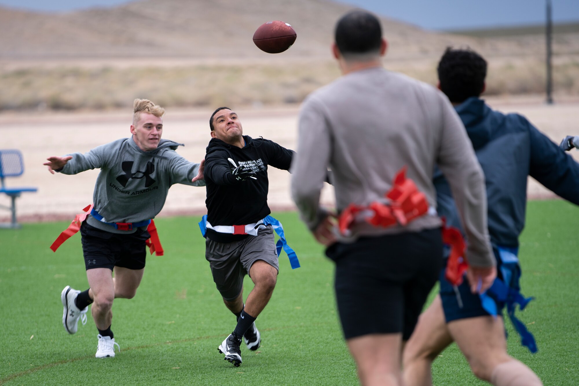 An airman catches a football while being defended by other Airmen on a turf field during a flag football game.