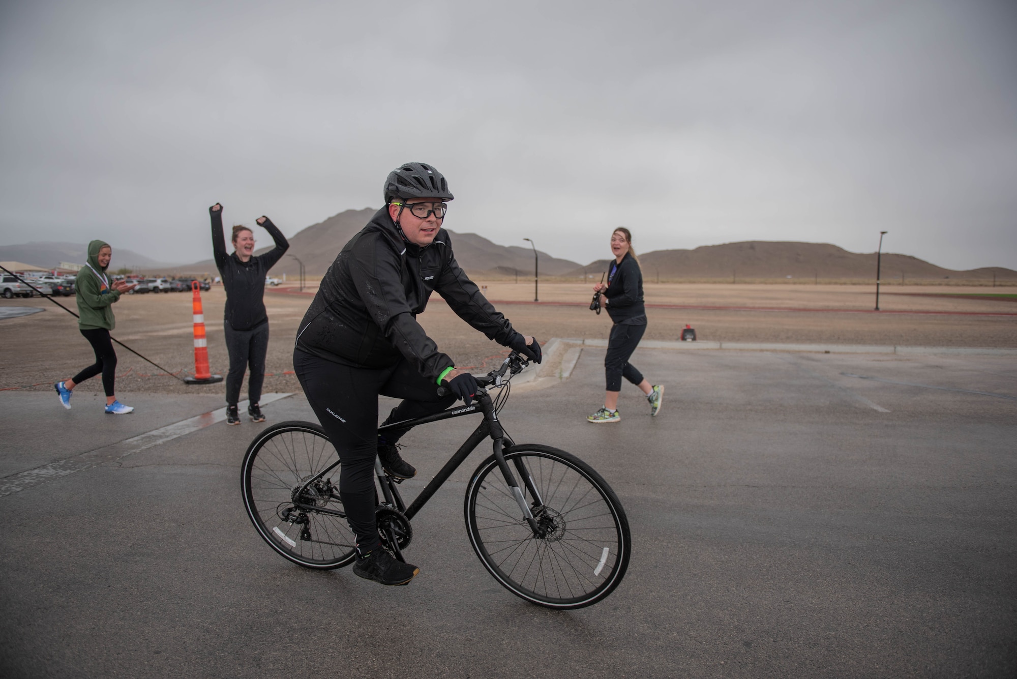 An airman rides past the finish line on a bike while more Airmen cheer him on.