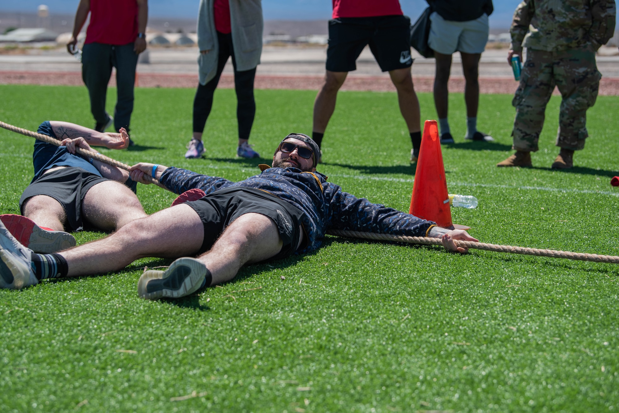 An airman lays on a turf field after falling to the ground during a tug of war match.