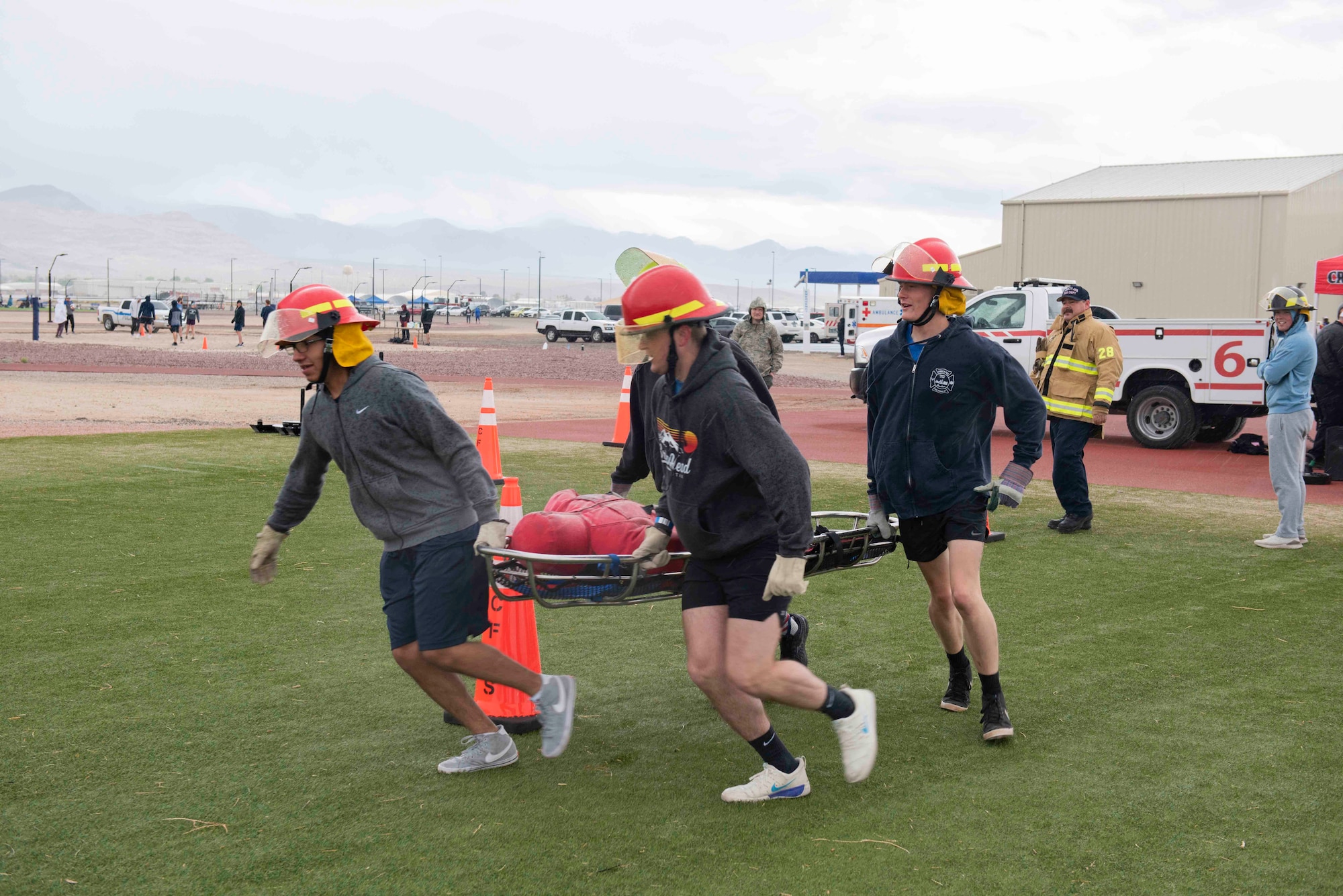 Four Airmen carry a stretcher around an orange cone during a fire muster competition on a turf field.