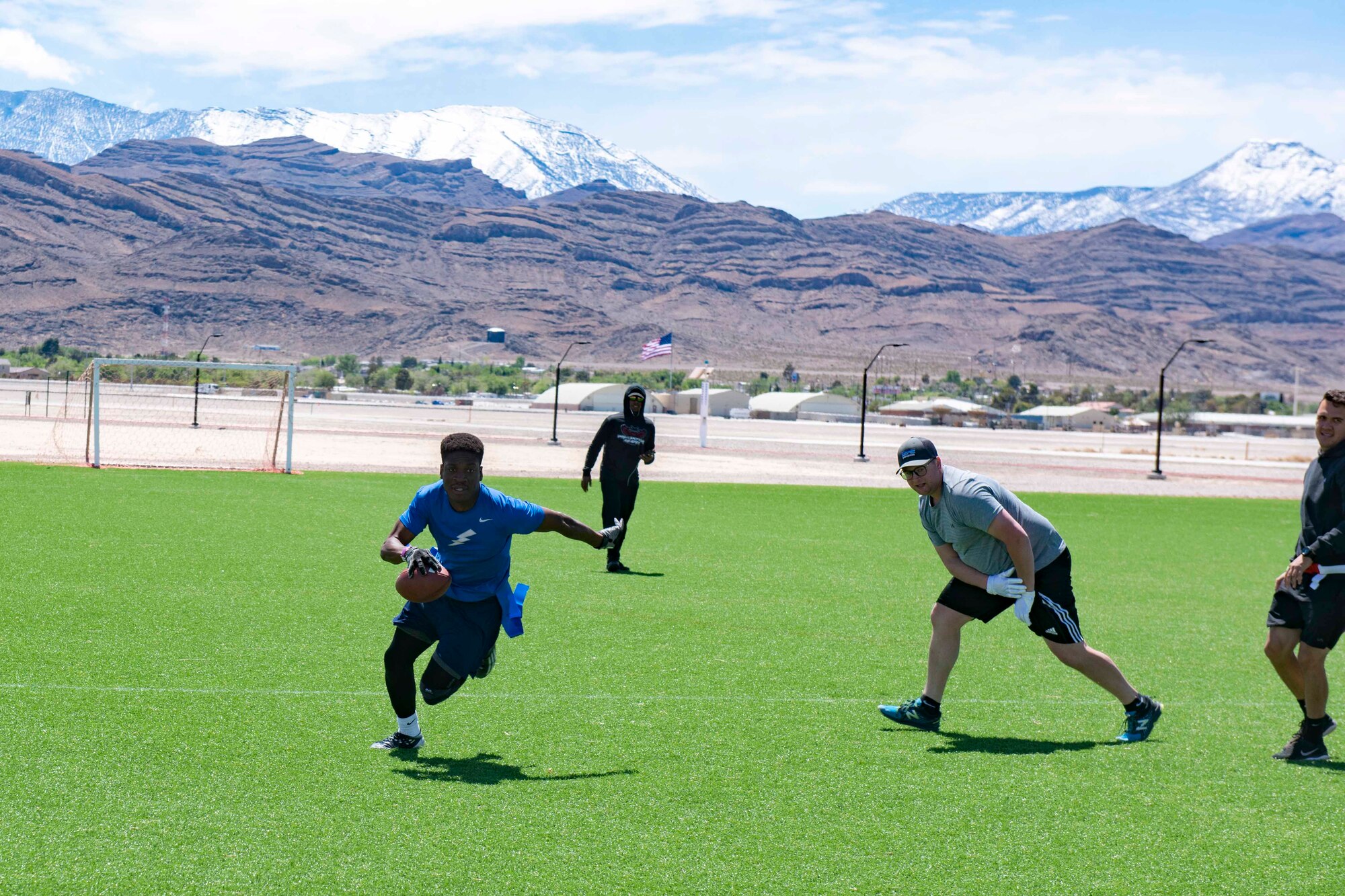 An airman sprints with a football on a turf field during a flag football game.